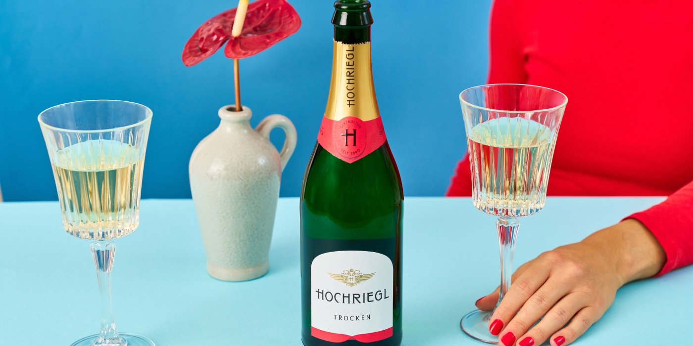 Dame sitzt mit Hochriegl und 2 Gläsern am Tisch