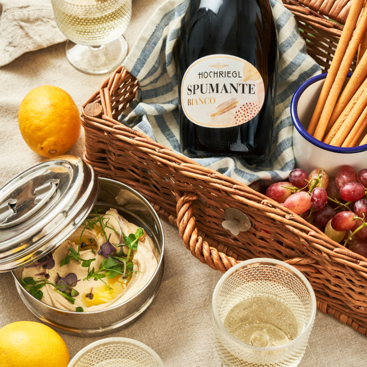 Flasch Spumante Bianco liegt im Picknickkorb mit Weintruaben und Hummus