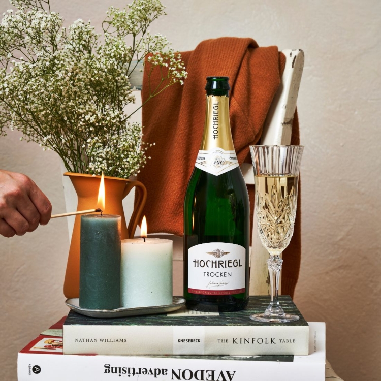 Flasche Hochriegl Trocken steht auf einem Buch, eine Person zündet eine Kerze an